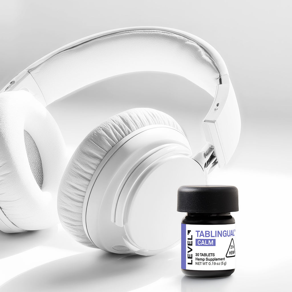 White headphones and a small bottle labeled 'LEVEL CALM' on a light gray background